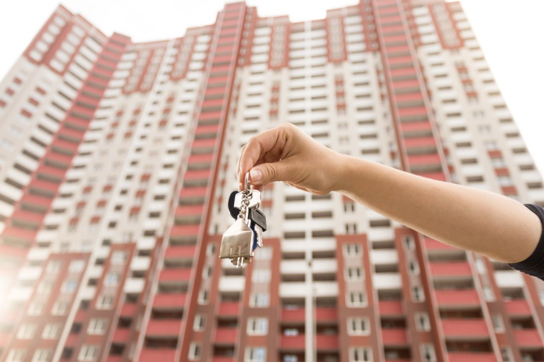 mano con llaves delante de un edificio de viviendas